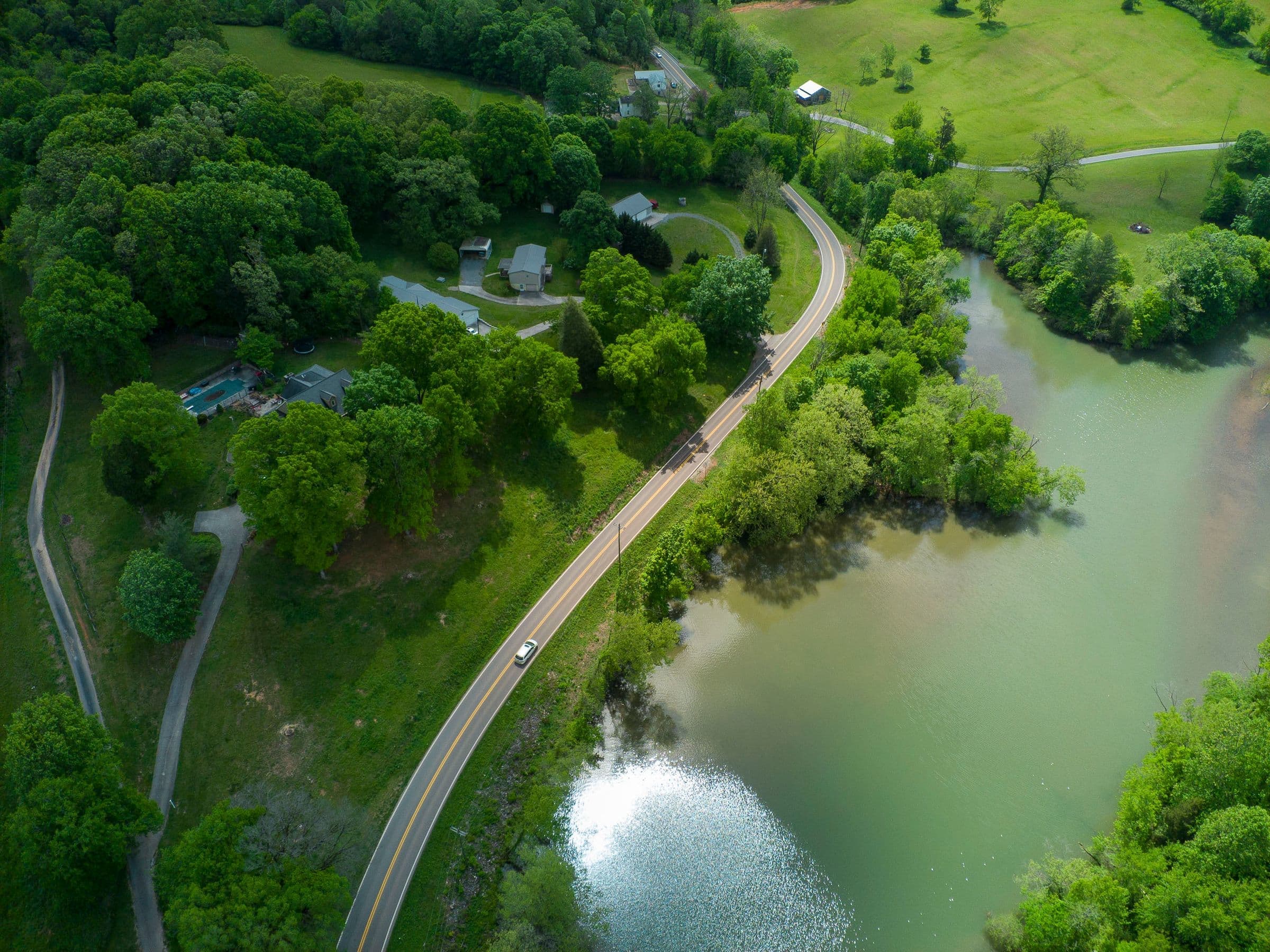 Junk removal in Loudon, TN: overhead view of a two-lane road beside a lake with houses, woods and pasture in Loudon, Tennessee