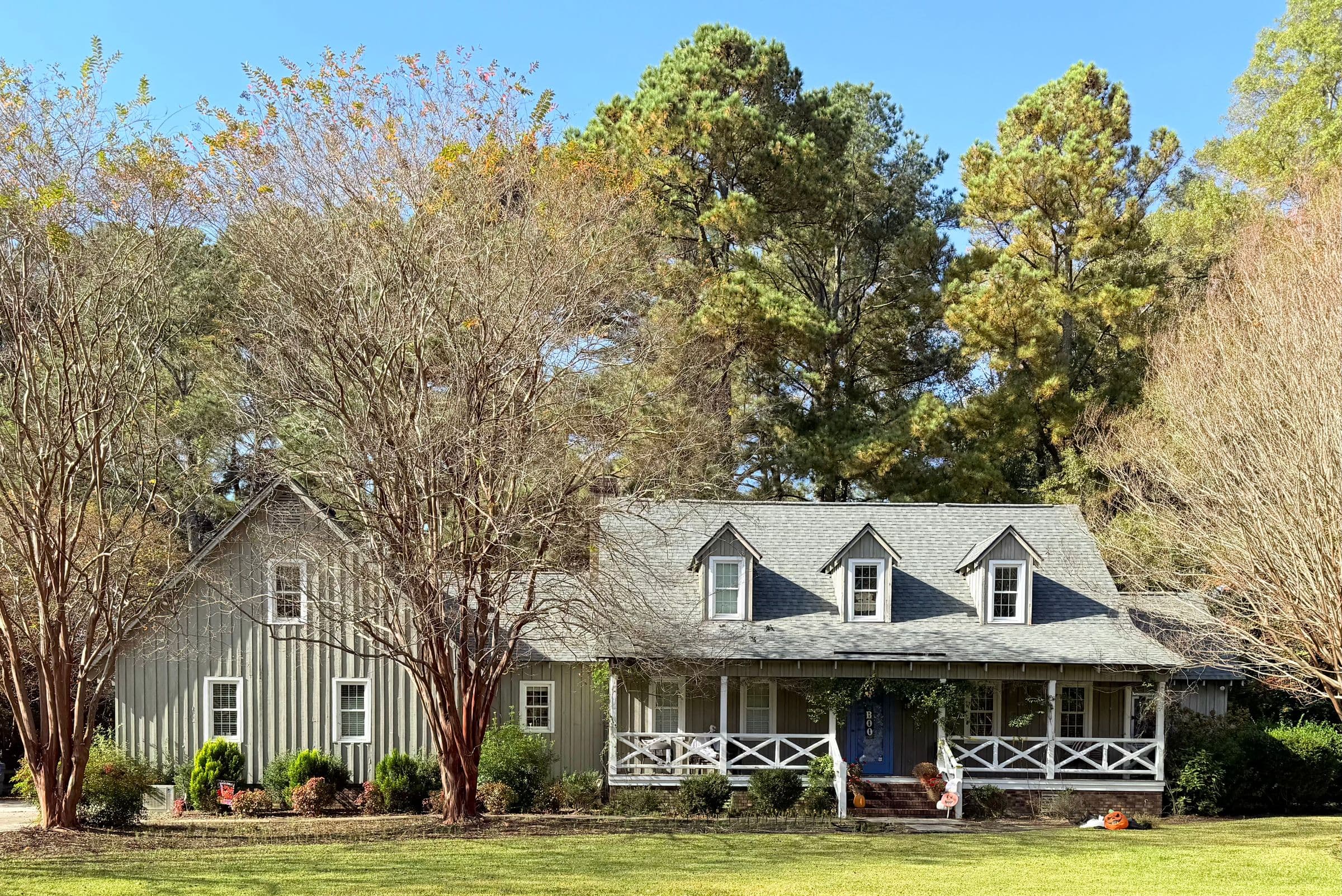 Junk removal in Maryville, TN: gray two-story house with a covered front porch, crape myrtles and tall pines on a wide lawn